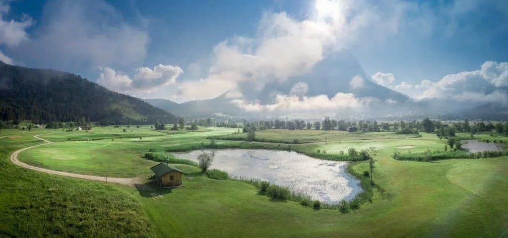 Green valley with pond, cloudy mountain and blue sky