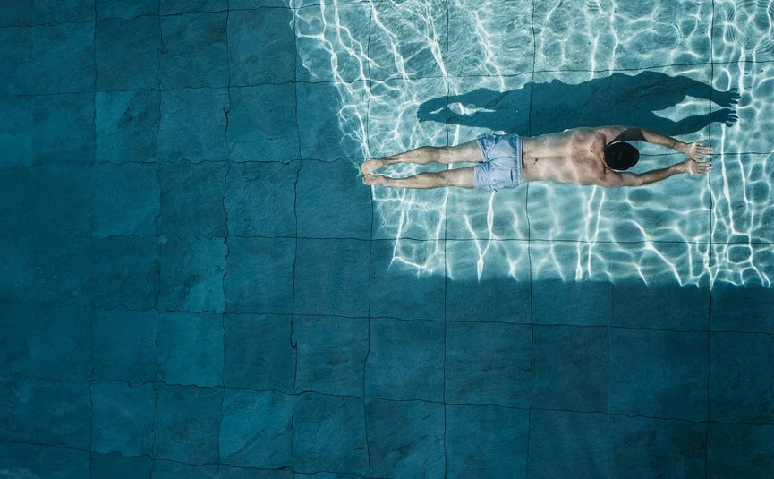 Mann schwimmt auf dem Bauch in klarem Wasser eines Pools mit Kacheln