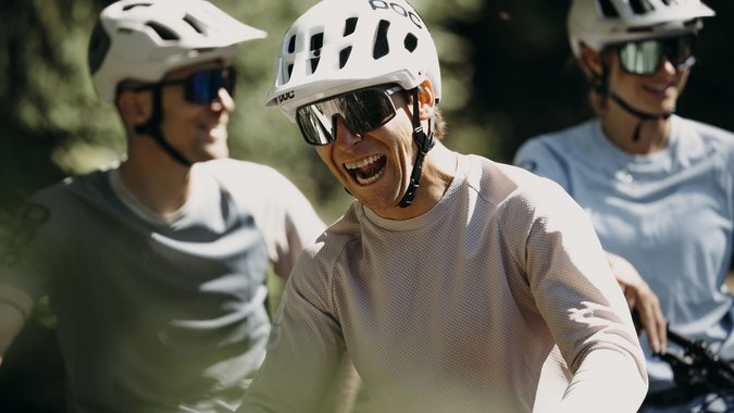 Drei Radfahrer mit Helmen und Sonnenbrillen lachen zusammen im Freien