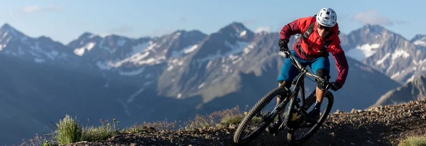 Mountain biker riding on a mountain trail with alpine peaks in the background