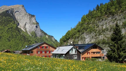Alpenhütte mit gelben Blumenfeld und steilen Felsen unter klarem blauem Himmel