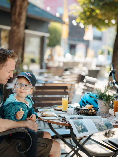 Vater und Tochter sitzen draußen an einem Cafétisch und essen gemeinsam.