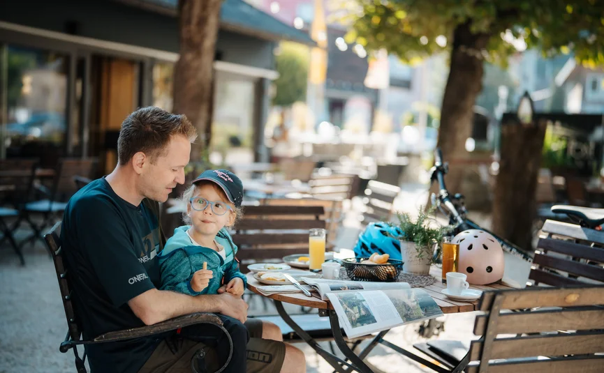 Vater und Tochter sitzen draußen an einem Cafétisch und essen gemeinsam.