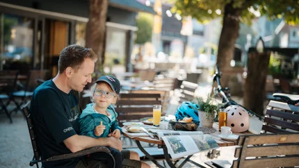 Vater und Tochter sitzen draußen an einem Cafétisch und essen gemeinsam.
