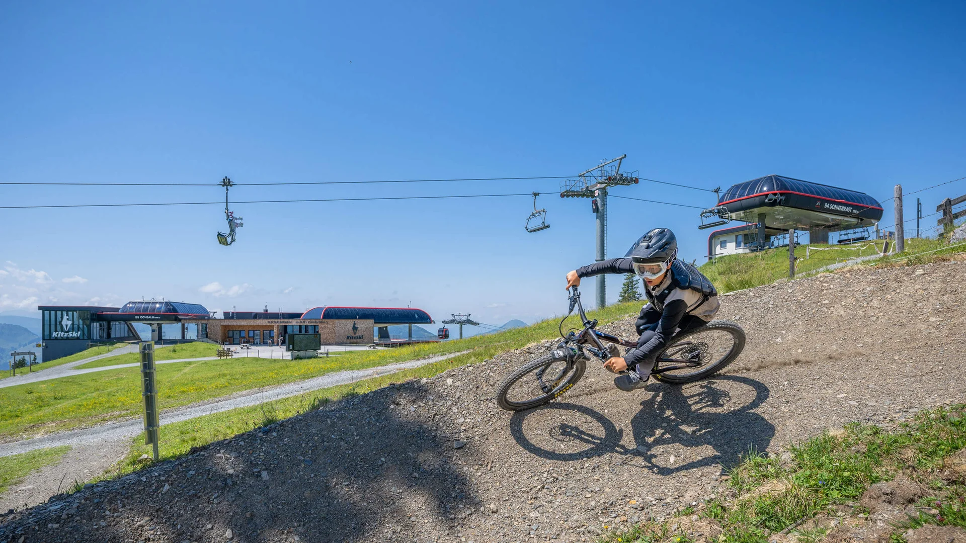 Mountainbiker fährt auf einem Trail mit Sessellift und Bergstation im Hintergrund