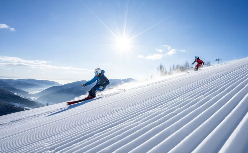 Twee skiërs dalen een vers geprepareerde piste af in fel zonlicht