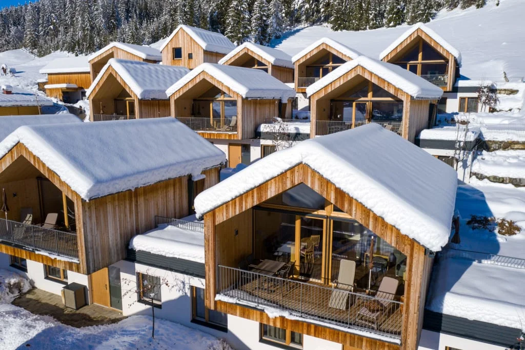 Verschneite Holzhäuser in einem Winterresort, umgeben von verschneiten Bergen