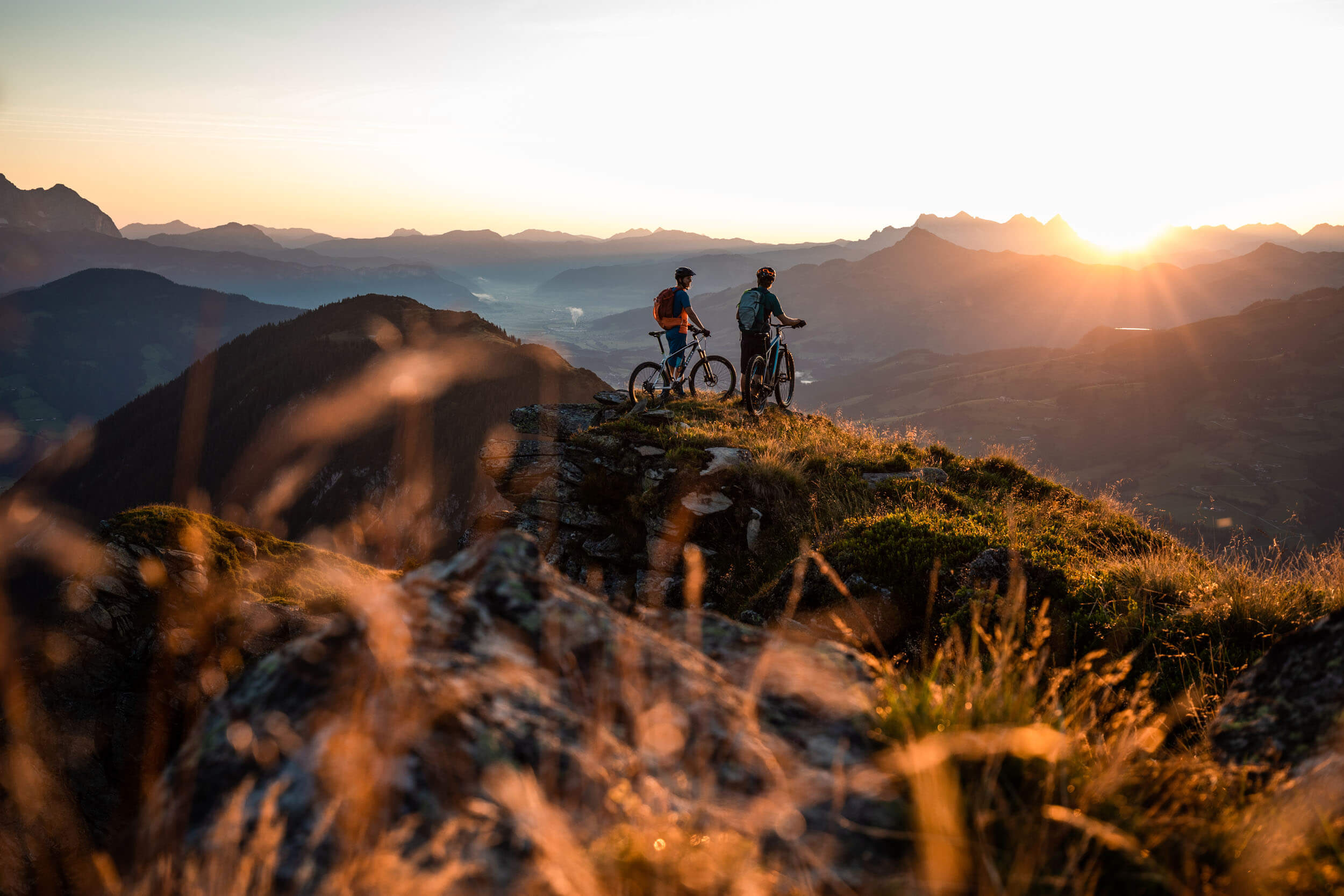 Two mountain bikers on a summit watching the sunset