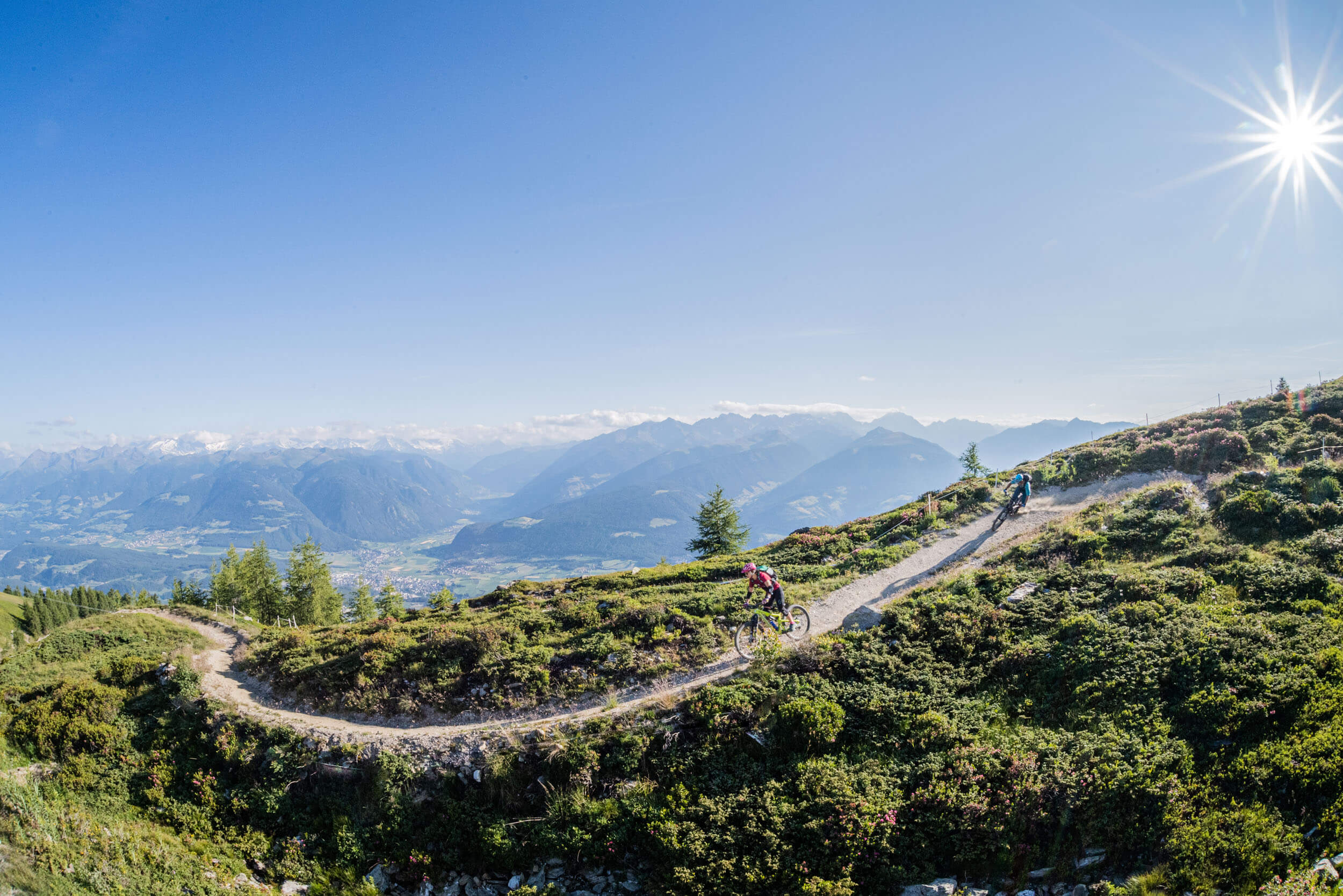 Mountainbiker fahren auf einem Bergpfad mit Alpenpanorama bei sonnigem Wetter