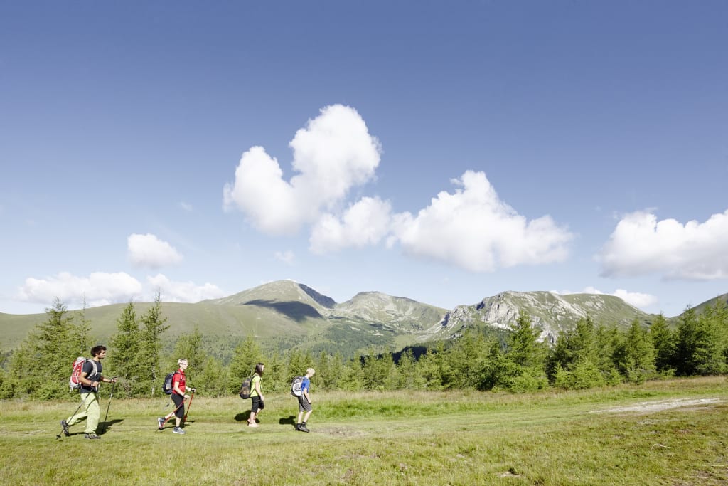 Vier Wanderer mit Rucksäcken in einer Berglandschaft bei klarem Himmel