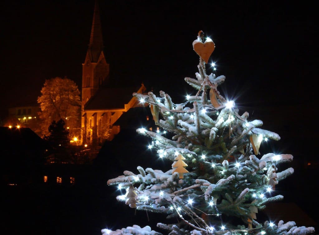 Weihnachtszauber Weihnachtsbaum mit Lichterkette und Schnee bei Nacht vor einer Kirche
