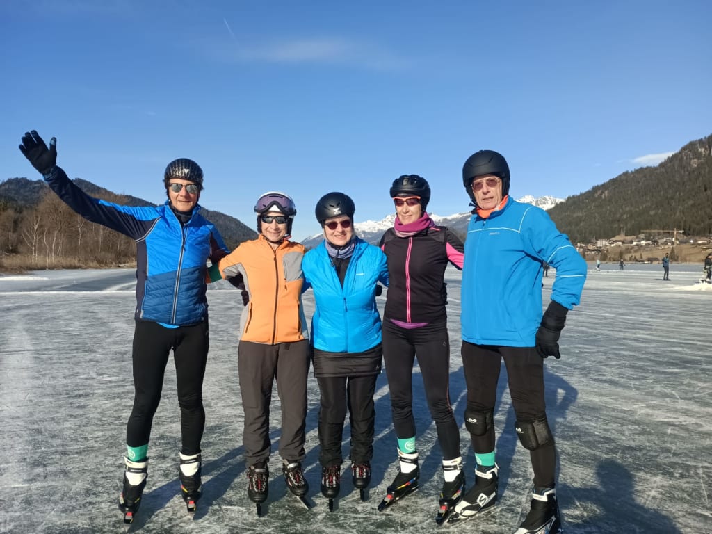 Regitnigs Eislauf-Wochen Fünf Personen posieren auf Schlittschuhen auf zugefrorenem See mit Bergen im Hintergrund