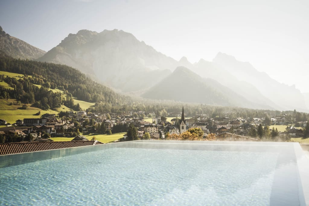 View of a heated infinity pool with mountains and village in the background