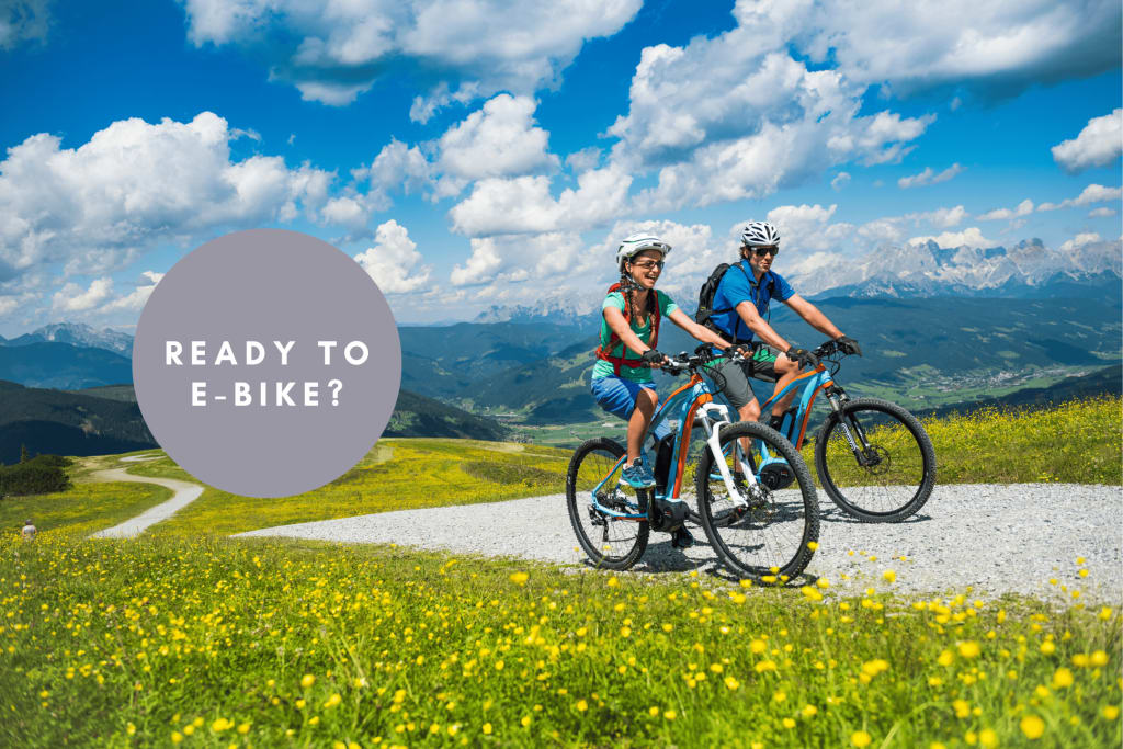 Zwei Personen fahren mit E-Bikes auf einem Bergweg bei schönem Wetter