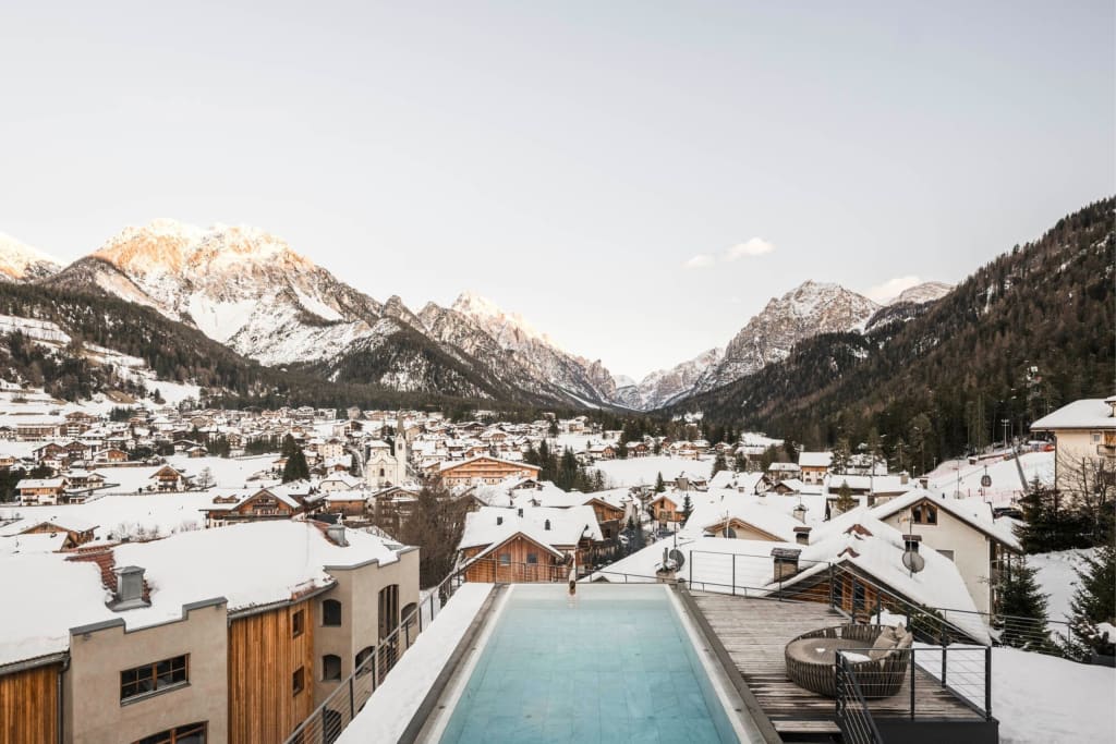 Dolomiti Spring Days S | 4=3 Sneeuwbedekt bergdorp met zwembad en bergen op de achtergrond