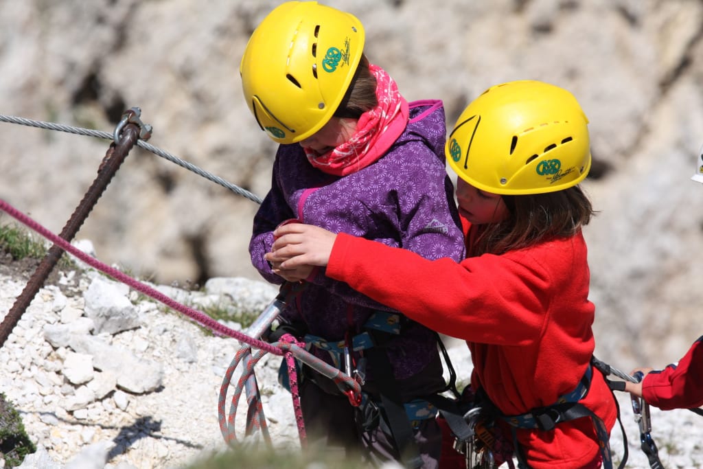 Dolomiten Abenteuerwoche Kinder mit Helmen beim Klettern, ein Kind sichert das andere