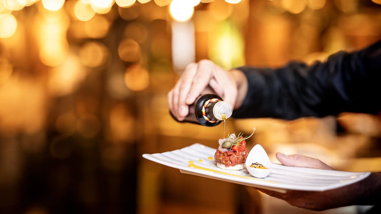 Hand giet olie over een kunstig opgediend gerecht op een wit bord