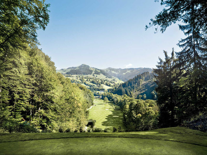 Green golf course surrounded by trees with mountains in the background
