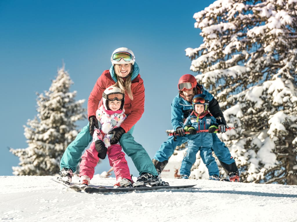 Ski-Familien-Woche Gezin leert skiën op besneeuwde piste met bomen op de achtergrond