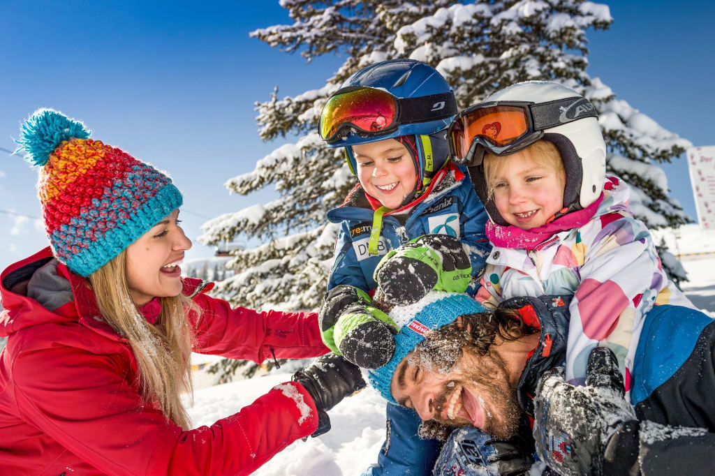 Ski-Familien-Woche Familie spielt lachend im Schnee bei sonnigem Wintertag