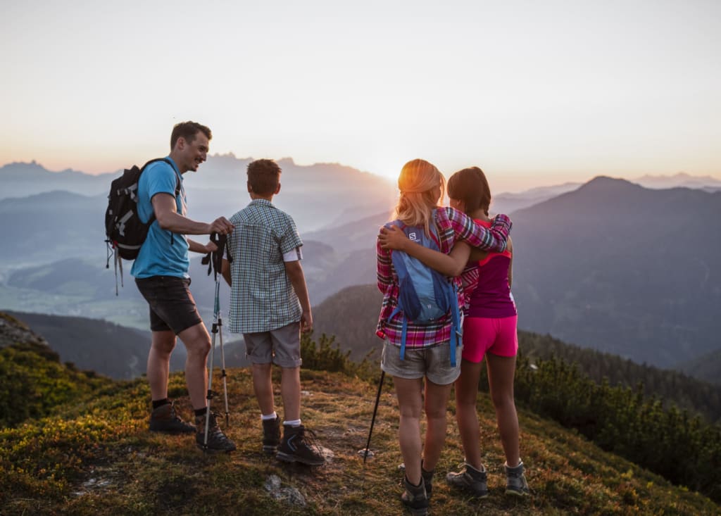 Vater und drei Kinder auf Berggipfel bei Sonnenuntergang beim Wandern