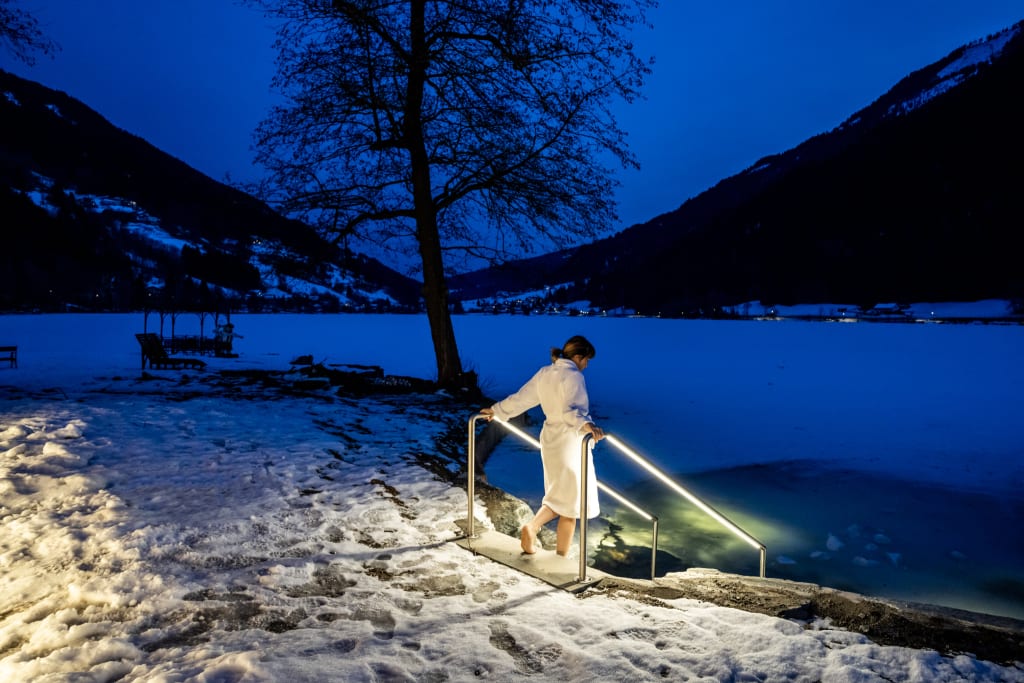 Woman in bathrobe entering icy lake at night with snowy shore