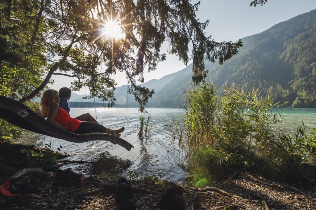 Kennenlerntage Juni Zwei Personen auf Schaukel am Seeufer mit Bergblick und Sonnenschein