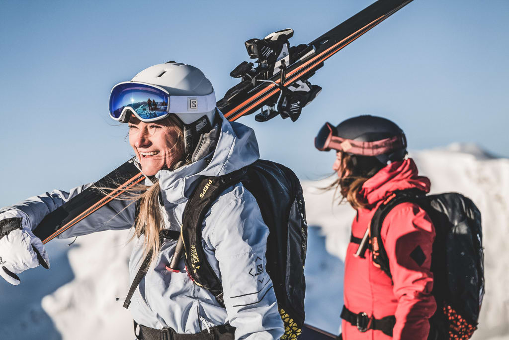 BRING A FRIEND - gratis 6 Tages-Skipass für die 2. Person Zwei Skifahrer in Winterkleidung mit Ausrüstung vor verschneiten Bergen