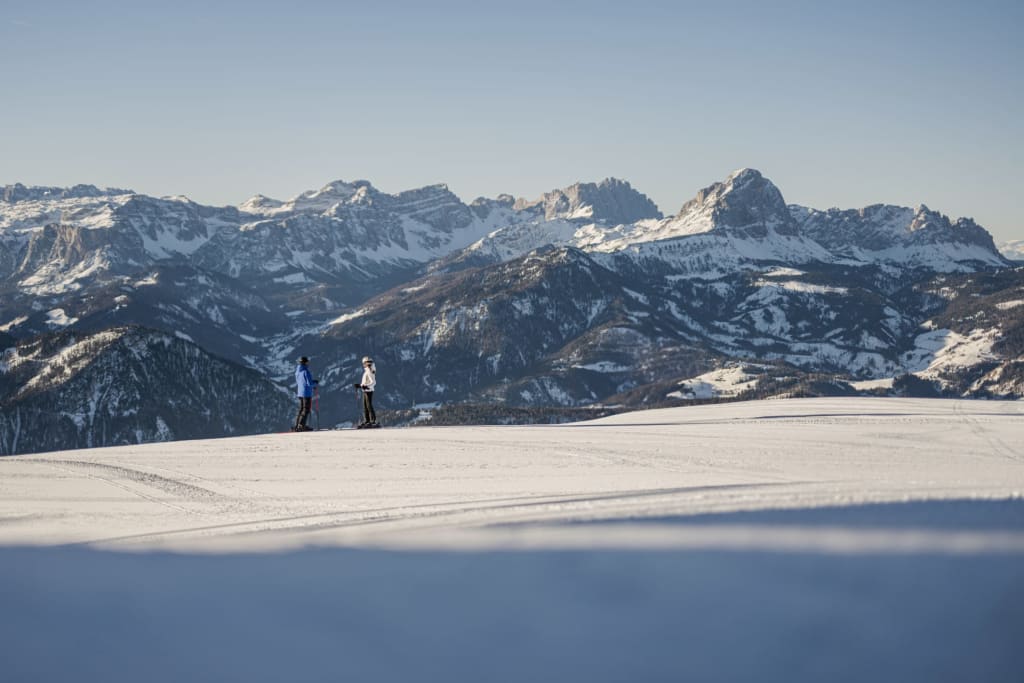 Ladin Winter Days - zwischen Ski & Tradition 🎭 Twee skiërs op een besneeuwde vlakte met besneeuwde bergen op de achtergrond