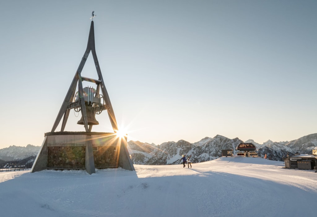 Bell tower and two people on snowy mountain at sunset
