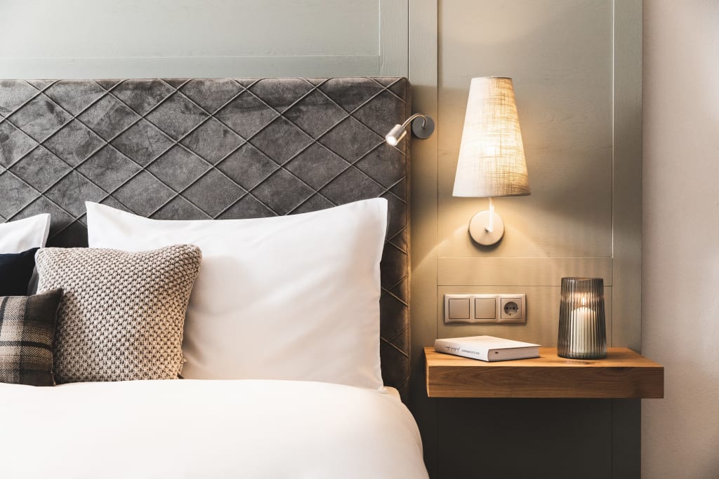 Alpines Doppelzimmer Deluxe Gemütliches Bett mit Zierkissen und Wandlampe neben einem Nachttisch