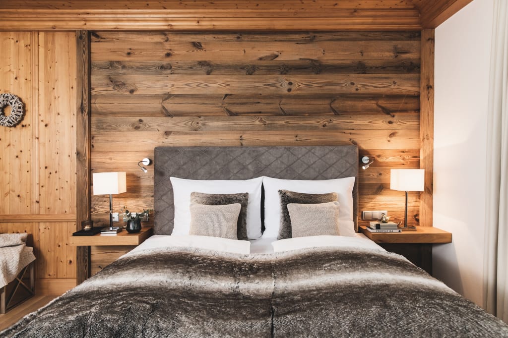 Alpine Junior Suite Gemütliches Schlafzimmer mit Holzwand, Lampen und flauschiger Bettdecke