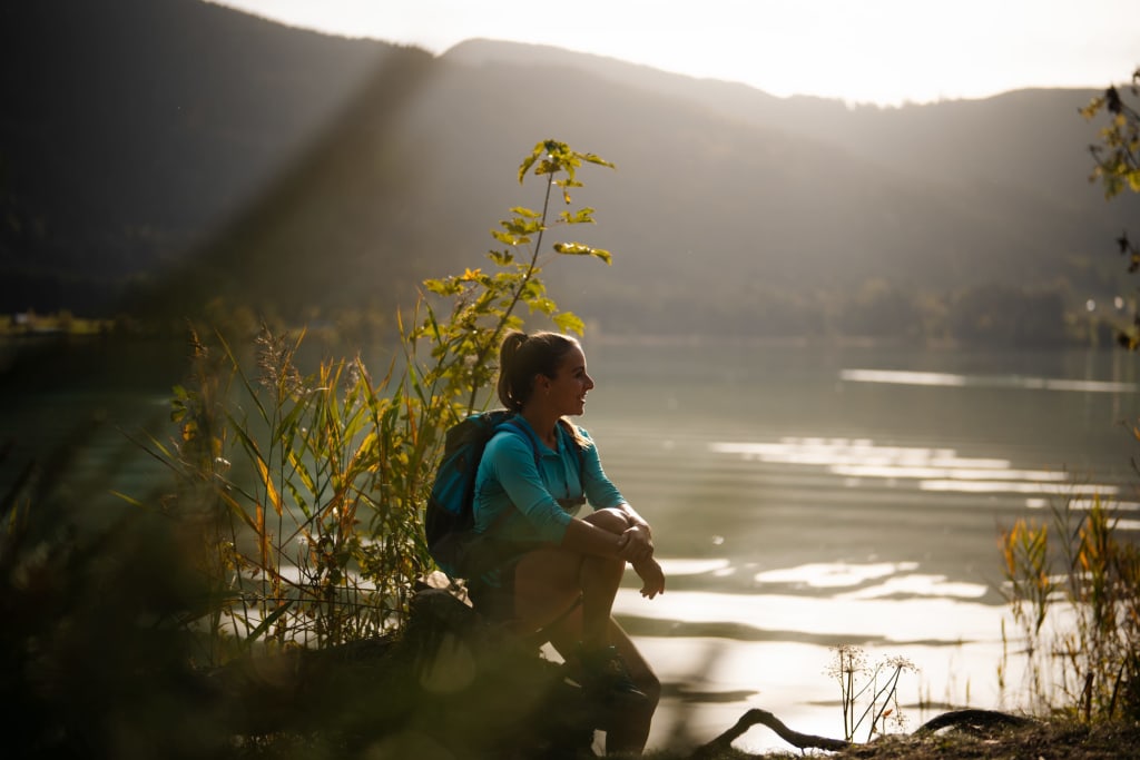 Leistungsfähig & gesund Frau mit Rucksack sitzt am Seeufer und genießt die Berglandschaft