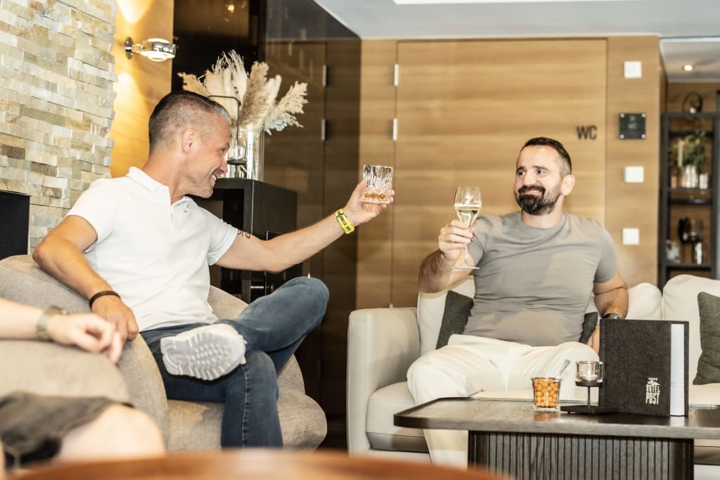 Mountainbike Woche Zwei Männer stoßen mit Getränken in einer gemütlichen Lounge an