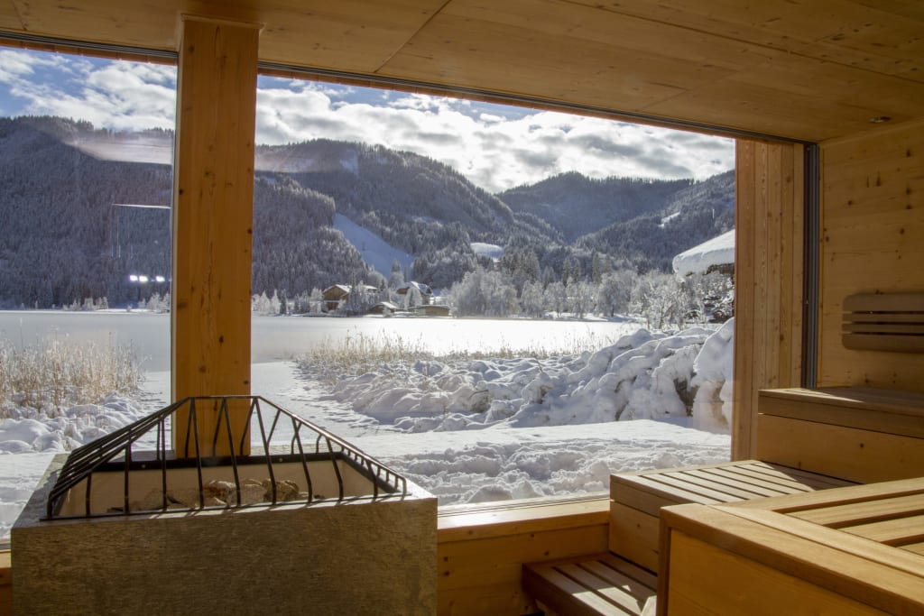 Blick aus einer Sauna auf schneebedeckte Berge und ein gefrorenes Seeufer