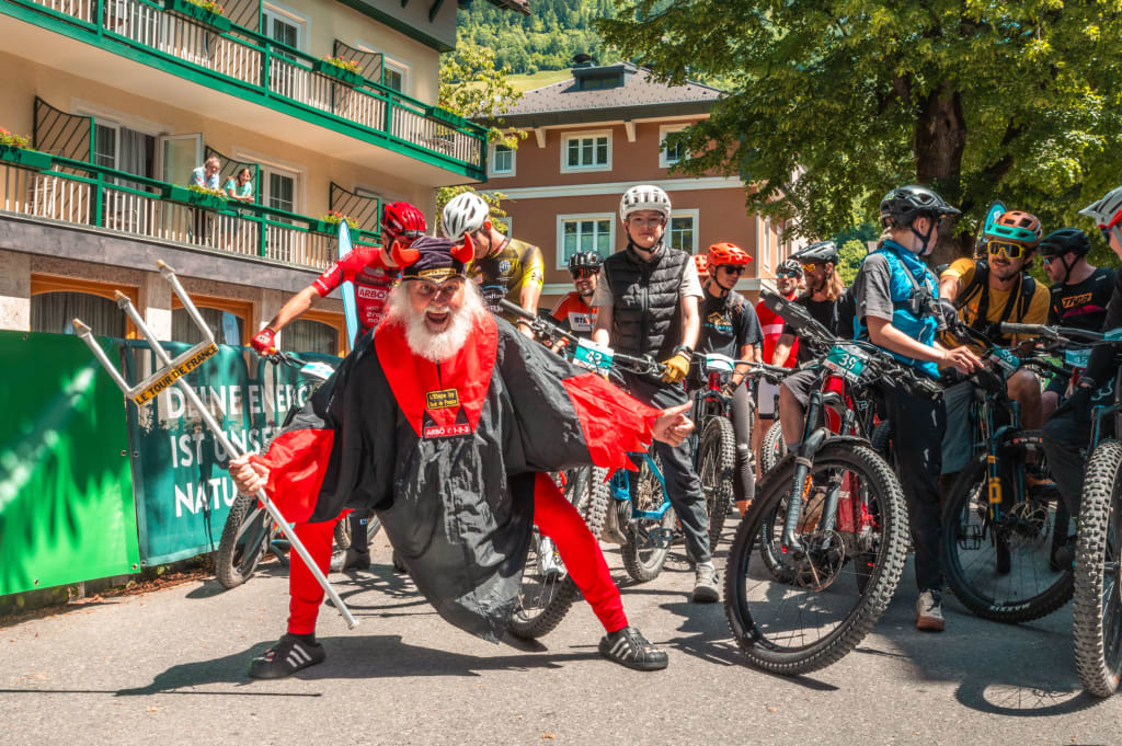 Man in devil costume posing in front of cyclists at an outdoor event