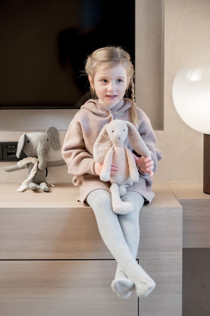 Mädchen sitzt mit einem Stoffhasen auf einem Holzregal