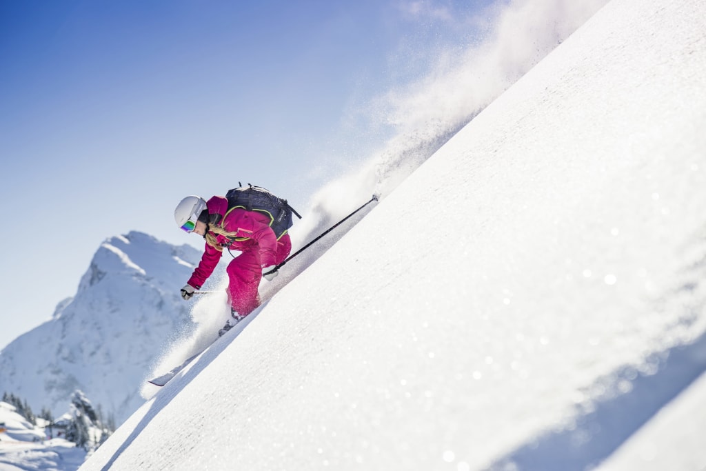 Pulverschnee-Wochen Skifahrerin in roter Kleidung fährt einen verschneiten Hang hinunter vor Bergkulisse