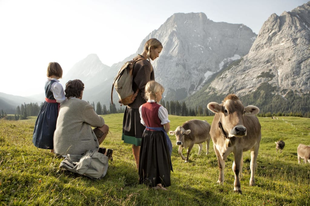 Familie kijkt naar koeien op een weiland met bergen op de achtergrond