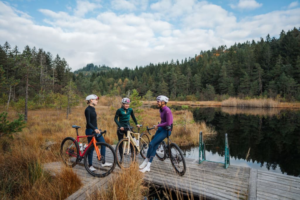 Three cyclists standing with bikes on a wooden pier by a lake in autumn forest