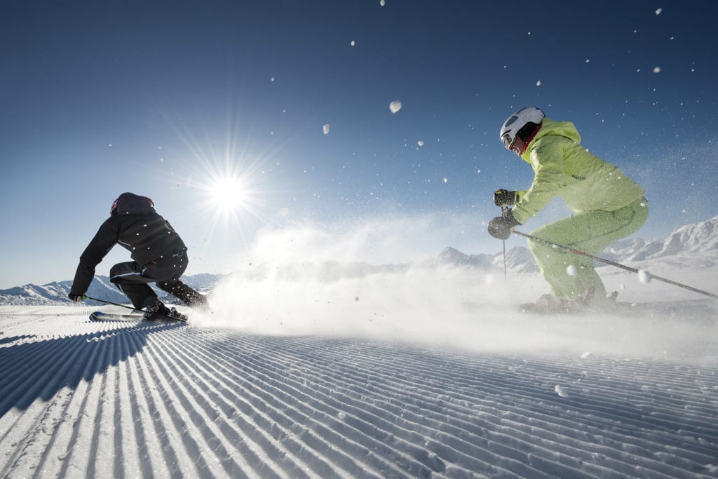 Two skiers skiing down a freshly groomed slope in sunny weather