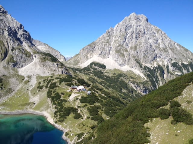 5=4 Tage Zugspitze Bergfrühling Berglandschaft mit klarem See und Berghütte unter blauem Himmel
