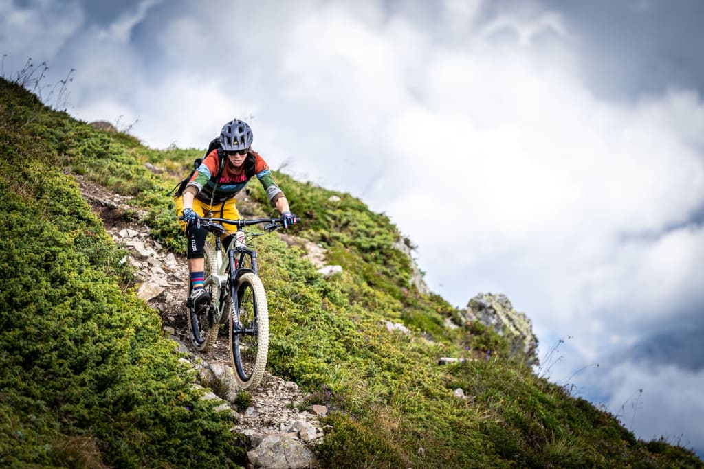 Mountainbiker fährt steilen, felsigen Pfad auf bewachsenem Hügel hinunter
