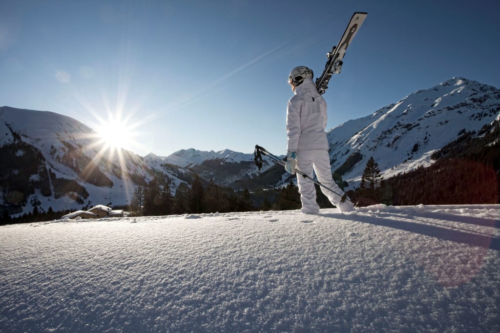 Skier carrying person stands on snow looking at mountains during sunset