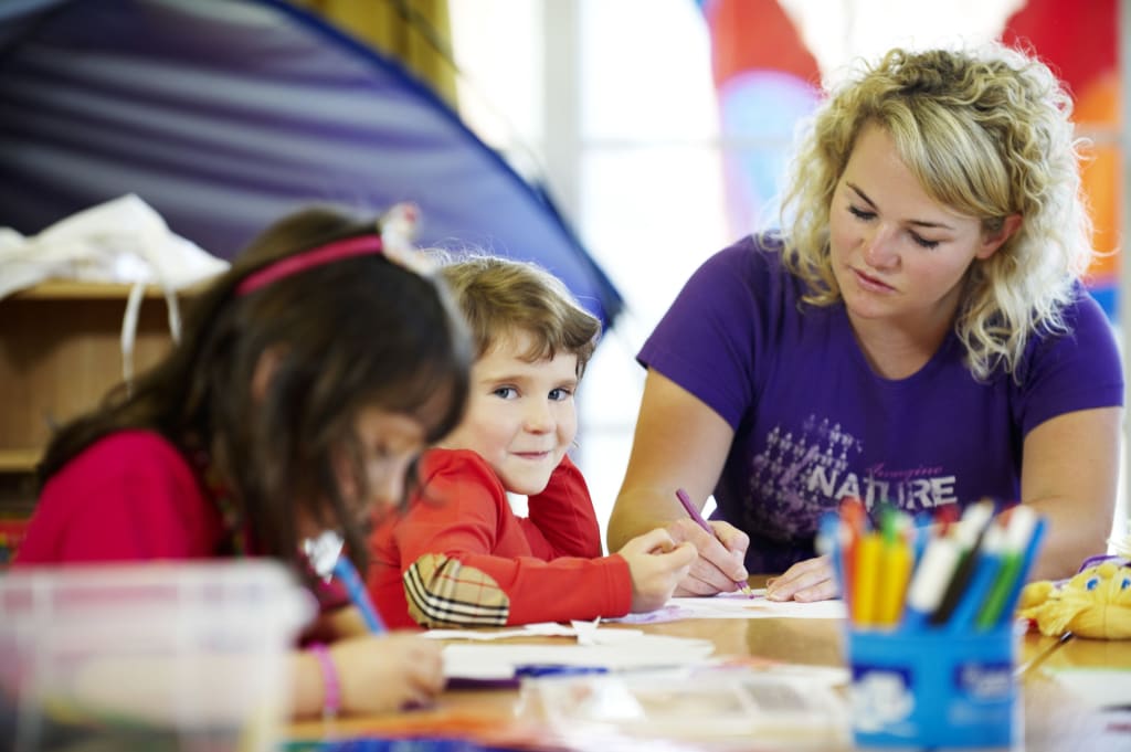 Pedagoog en kinderen tekenen samen aan tafel op de kleuterschool