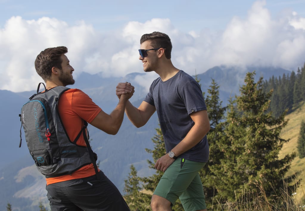 Adam & Adam meet eva, Zwei Männer grüßen sich beim Wandern in den Bergen mit Handschlag.
