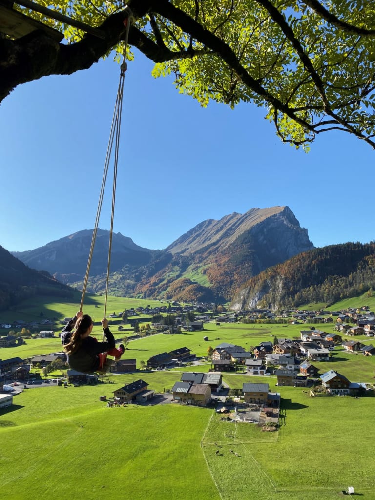 Child swings high above a green valley with mountains in the background