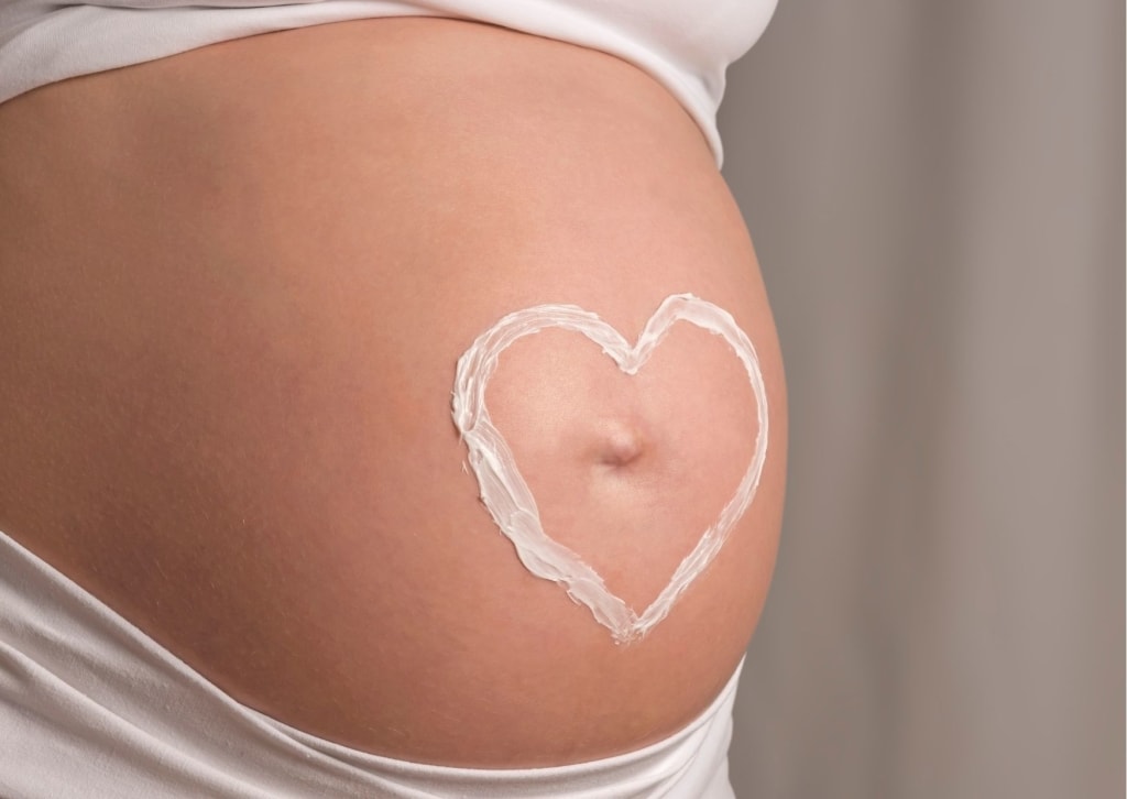 Babymoon Schwangerer Bauch mit Herz aus Creme auf der Haut