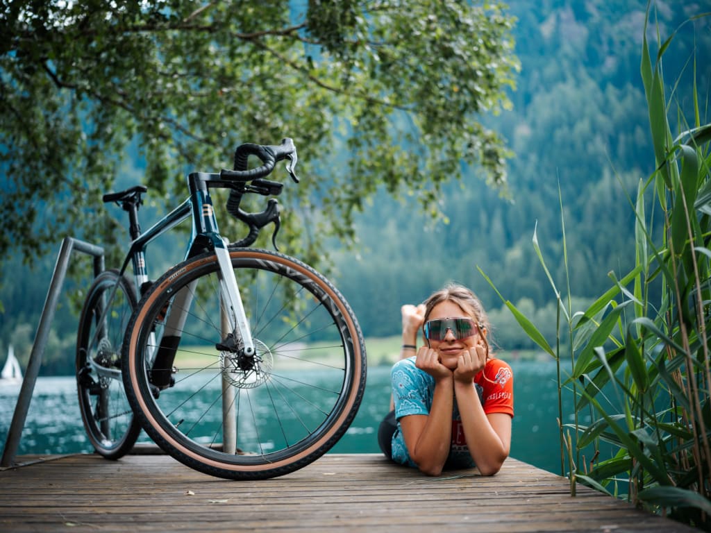 Woman lying next to racing bike on wooden dock by lake with forest backdrop