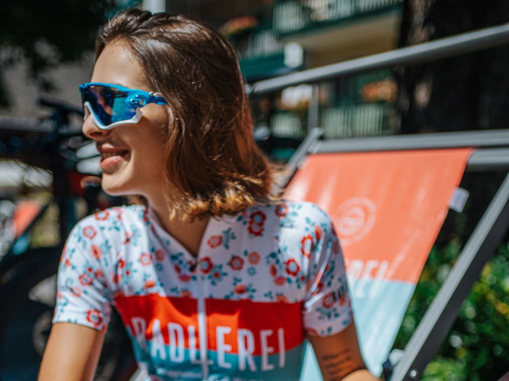 Frau mit Sonnenbrille und Radtrikot sitzt draußen und lächelt